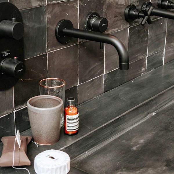 a black faucet with a black handle and a brown mug on a tile wall