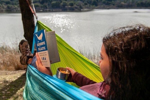 a woman reading a book in a hammock by a lake